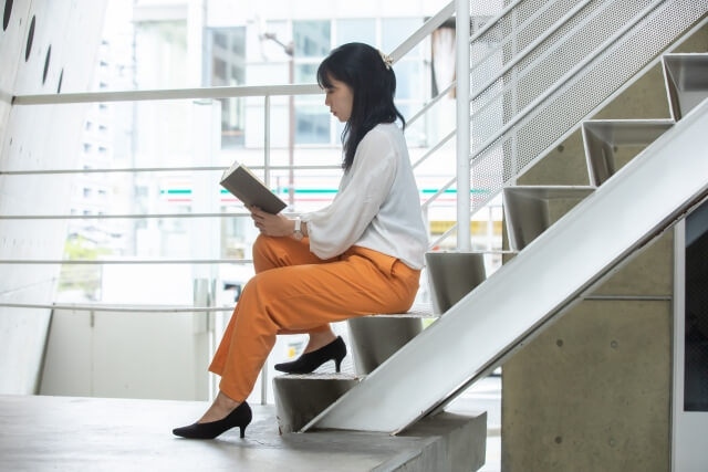 階段に座って姿勢よく読書する女性