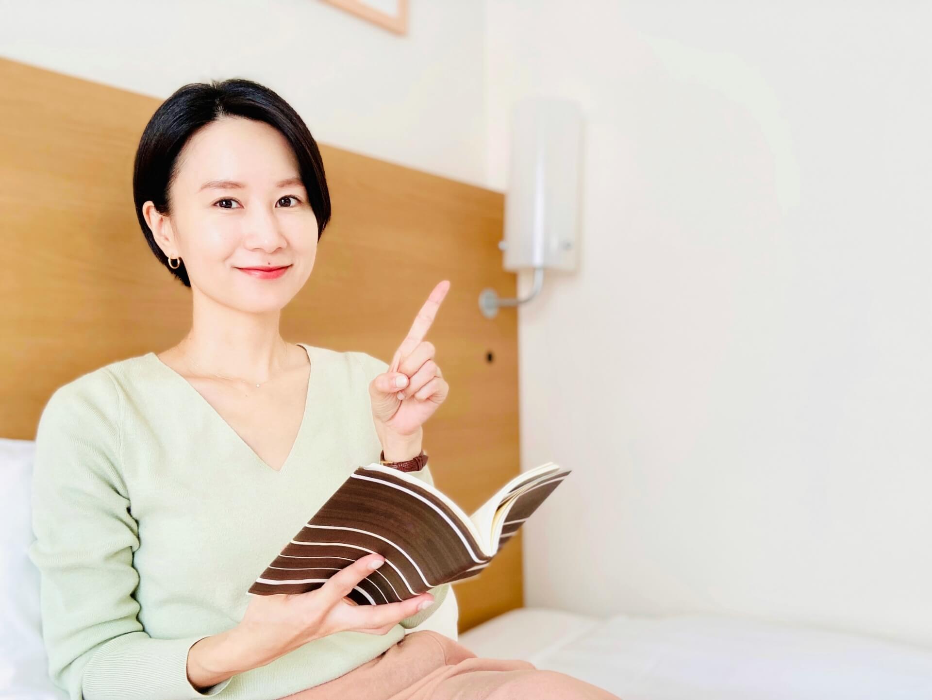 ベッドで本を読みながら説明する日本人女性