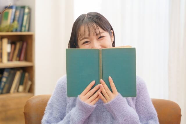 顔半分を本で隠す笑顔の女性