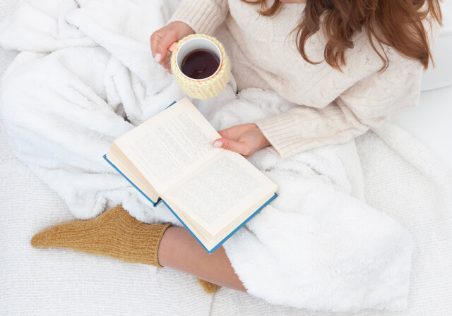 ベッドに座って本を読みながらコーヒーを飲む女性1